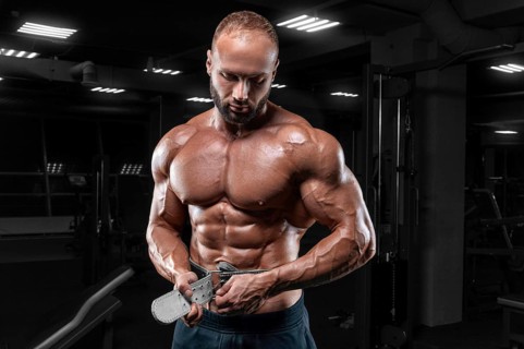 The athlete poses in the gym with an athletic belt. Fitness