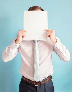 Anonymous businessman covers his head using a blank sheet to hide face expression. Incognito business person hidden behind a white empty paper