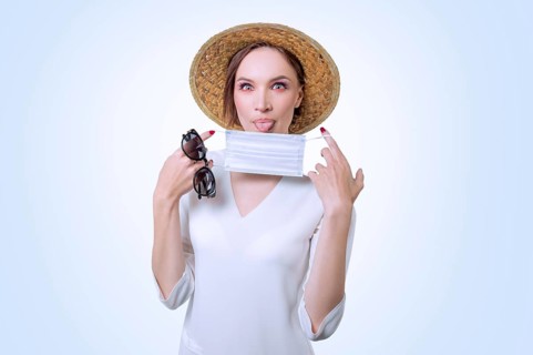 Beautiful girl posing on a white background in a yellow hat. She has a medical mask in her hands. The concept of tourism during the epidemic.