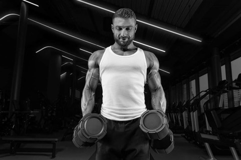 Handsome young man working out with dumbbells in the gym. Shoulder pumping. Fitness and bodybuilding concept.