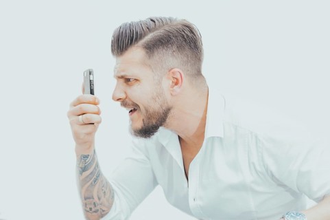 Man in a shirt looks at the smartphone screen in surprise. Concept of unsuccessful betting on games
