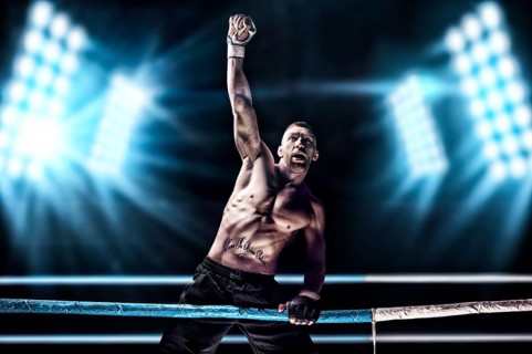 Kickboxer posing in the ring. The athlete climbed the ropes and took a victorious position against the background of spotlights. The concept of mma