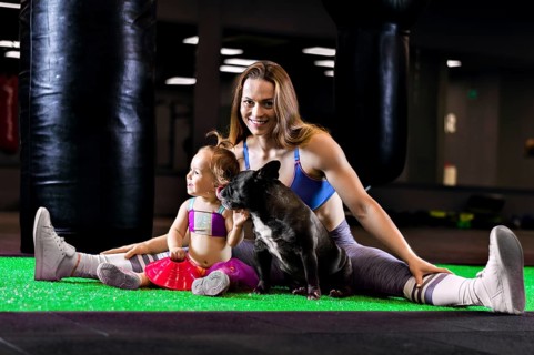 Charming sports mom trains in the gym with her little daughter and a French bulldog.