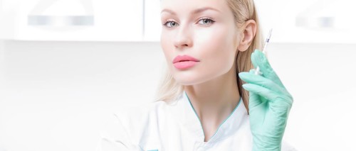 Portrait of a blonde girl in a medical gown with a syringe in her hands. Vaccination concept.