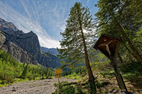 An idyllic mountain landscape with signposts and a wooden cross under a clear blue sky