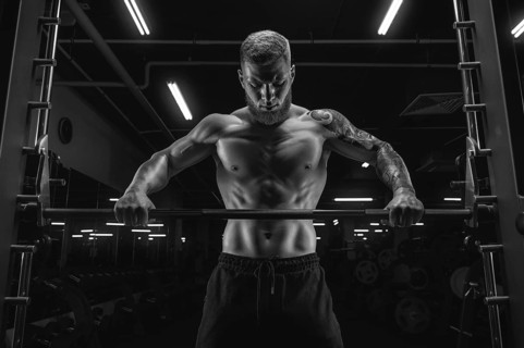 Portrait of an athlete standing in front of a barbell in the gym. Bodybuilding and fitness concept.