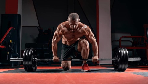 Athlete is standing on his knee and near the bar in the gym and is preparing to make a deadlift.