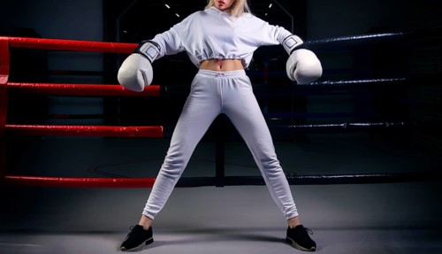 Charming girl in a white sweatshirt poses with huge white gloves against the background of a boxing ring. The concept of sports