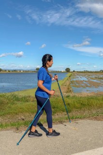 A woman in a blue shirt Nordic walking along a waterway on a sunny day with a clear blue sky