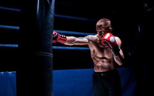 Professional boxer hits the bag against the background of the ring. Side view. The concept of sport and classic boxing.