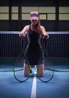Portrait of a beautiful tennis player posing with two rackets on the court. Sports concept.