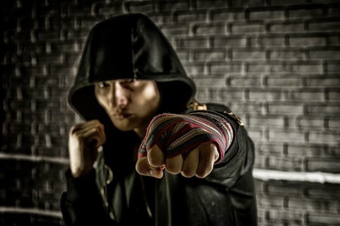 Boxer in a black sweatshirt and bandages wound on his hands beats his fist forward. The concept of sports