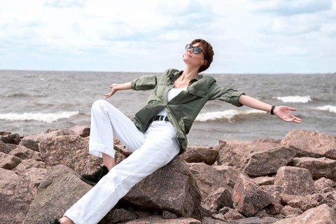 Portrait of a stylish woman sitting on stones in the bay. Windy weather. Happiness