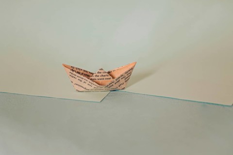 A simple origami paper boat on a diagonal split background with blue hues