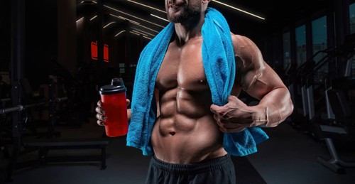 Portrait of a muscular guy with a naked torso and abs. Gym. Blue towel and red shaker. Fitness concept