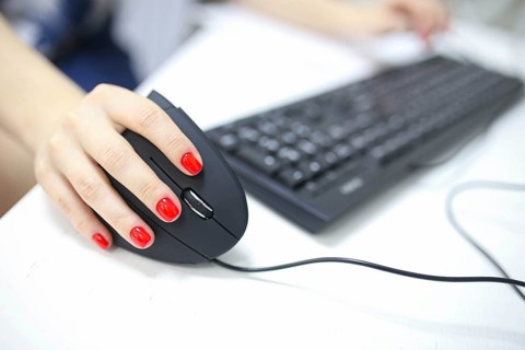 Girl's hand uses a vertical ergonomic joystick of a computer mouse. working at the computer