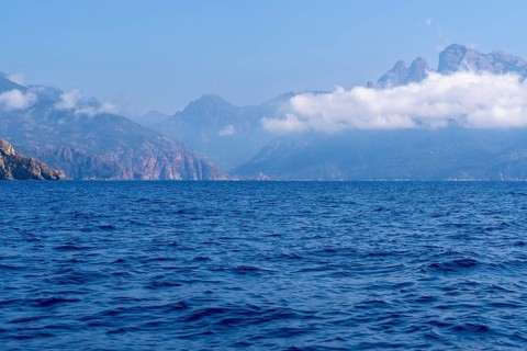 A calm seascape with mountains in the background and clouds in the sky