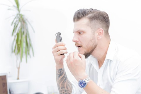 Man in a shirt looks at the smartphone screen in surprise. Concept of unsuccessful betting on games