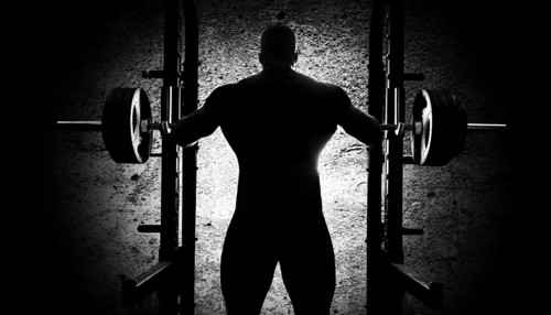 The weightlifter stands with his hands behind the heavy barbell. Back view