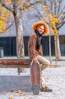 Vertical portrait of the side view of an alternative adult man with a skate in an urban park in autumn