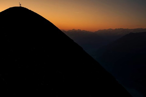 Mountaineer on ridge with Swiss mountains in the background at sunrise