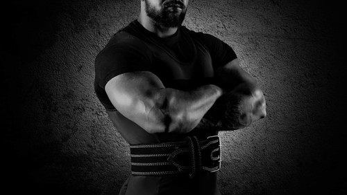 The weightlifter stands in a menacing pose with crossed huge arms and looks at the camera