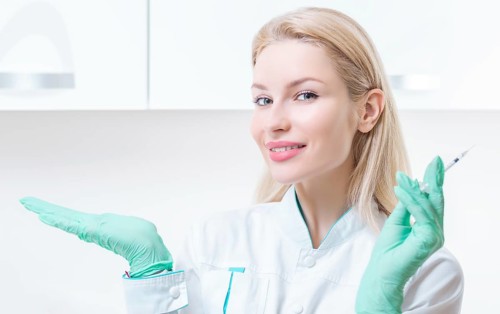 Portrait of a blonde girl in a medical gown with a syringe in her hands. Vaccination concept.