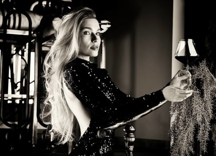 Seductive blonde in a green evening dress posing with a glass of red wine.