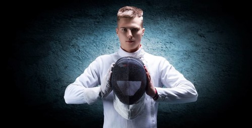 Portrait of a male fencer against a blue spot on the wall. He holds a helmet in front of him. The concept of fencing.