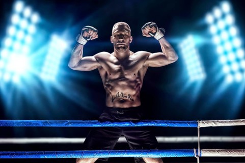 Kickboxer posing in the ring. The athlete climbed the ropes and took a victorious position against the background of spotlights. The concept of mma