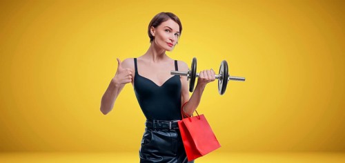 Beautiful slender woman posing in the studio with a dumbbell and gift bags. Gift concept. Gym membership. Ok sign.