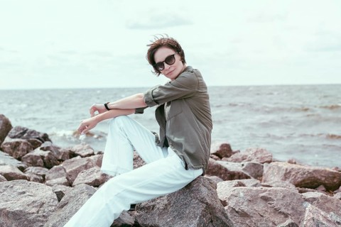 Portrait of a stylish woman sitting on stones in the bay. Windy weather. Happiness