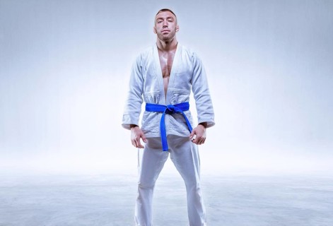 Athlete in a kimono with a blue belt stands on a light background. The concept of karate and judo.