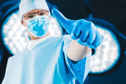 The doctor against the background of surgical lamps shows a raised finger. Medicine concept.