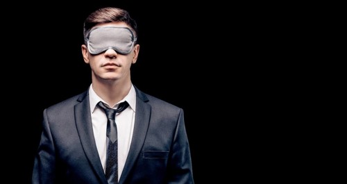 Portrait of a man in a mask for sleeping. He stands against a black wall. Blind business concept. Work during the crisis.