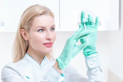 Portrait of a blonde girl in a medical gown with a syringe in her hands. Medical center advertisement.