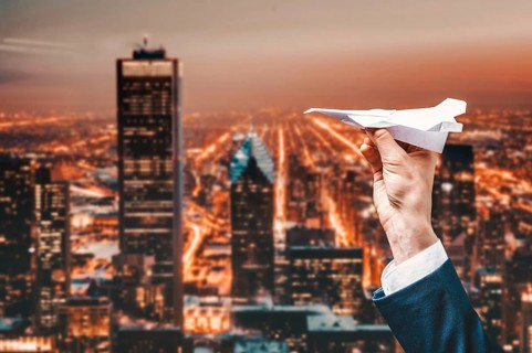 Image of a man's hand in a suit. He launches a paper airplane from the roof of a skyscraper. Business concept.