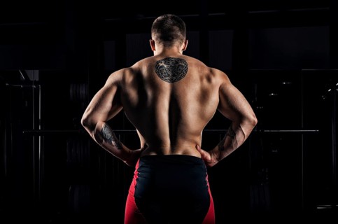 Huge weightlifter stands with his back to the camera and shows his huge back. Back view