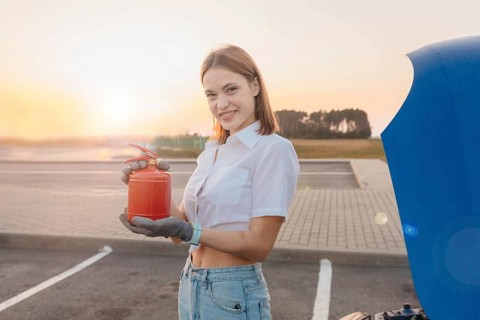 Young beautiful and hot woman driver holds a fire extinguisher in her hands