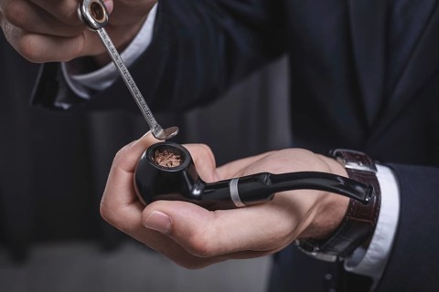 Image of male hands holding a smoking pipe and tamper. Tobacco smoking concept.