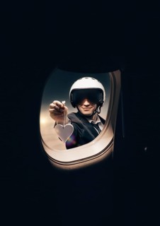 Portrait of a man in a helmet. He looks into the porthole of an airplane and holds out a heart-shaped figure. Travel and insurance concept.