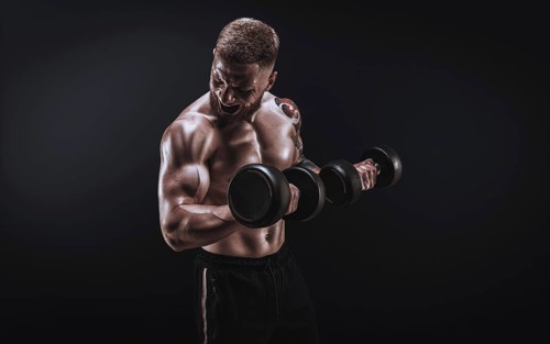 Young muscular guy pumping biceps with dumbbells. Concentrated flexion. Fitness and nutrition concept.