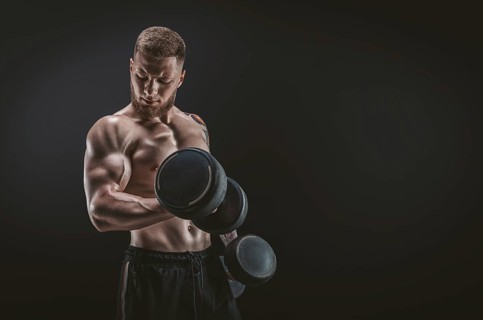 Young muscular guy pumping biceps with dumbbells. Concentrated flexion. Fitness and nutrition concept.
