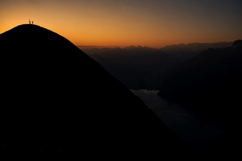 Mountaineer on ridge with Swiss mountains and Lake Thun in the background at sunrise