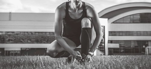 Portrait of a young runner who laces her boots at a football stadium. Sports concept.