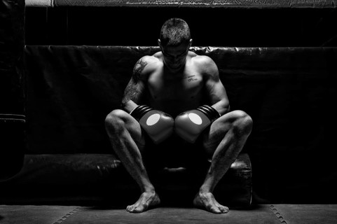 Boxer sits in gloves near the ring with his head bowed. The concept of sports