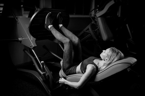 Charming blonde crouches in a hack machine. The concept of squat