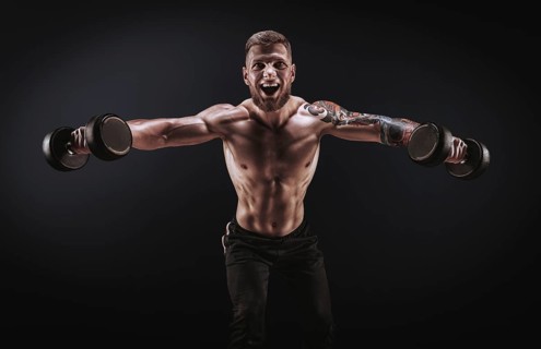 Handsome young man spreads his arms with dumbbells to the sides. Shoulder pumping. Fitness and bodybuilding concept.