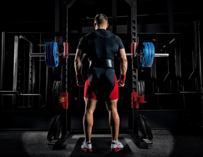 Professional athlete stands in front of the bars with a barbell and is about to crouch with her. Back view