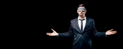 Portrait of a man in a mask for sleeping. He stands against a black wall. Blind business concept. Work during the crisis.